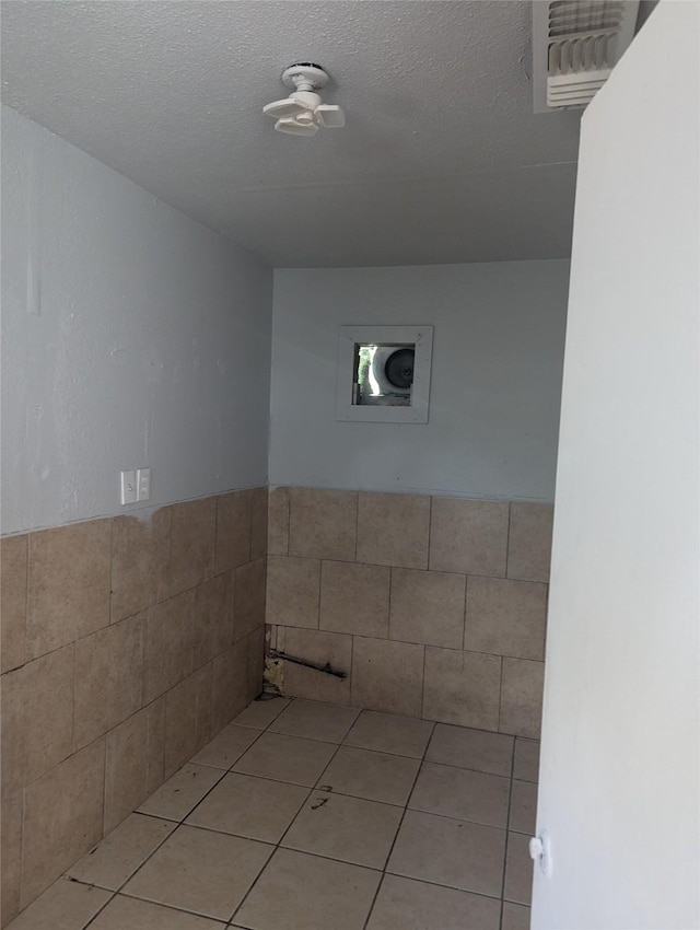 3108 Bideker Ave, Fort Worth, TX 76105 - bathroom with tile walls, tile patterned floors, a wainscoted wall, and a textured ceiling