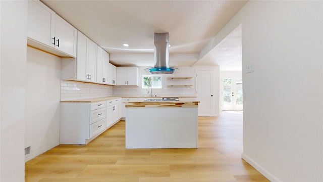 3809 Grover Ave, Fort Worth, TX 76106 - kitchen featuring island range hood, wooden counters, light wood-style flooring, white cabinetry, and backsplash