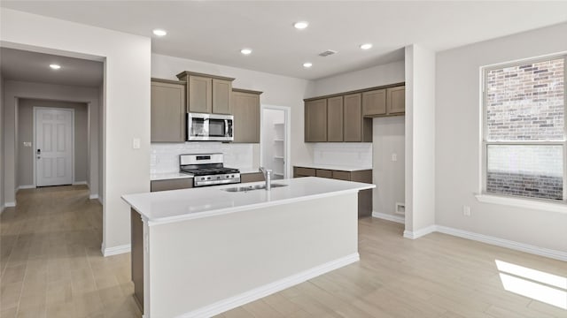 1109 Rushing Ct, Aubrey, TX 76227 - kitchen featuring appliances with stainless steel finishes, a sink, a kitchen island with sink, decorative backsplash, and light wood finished floors