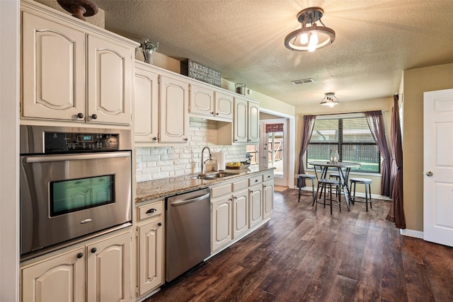 3701 Nocona Dr, Granbury, TX 76049 - kitchen with stainless steel appliances, a sink, a textured ceiling, backsplash, and dark wood-style floors