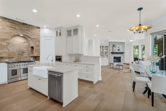6628 Castle Pines Dr, Plano, TX 75093 - kitchen featuring stainless steel appliances, a sink, a fireplace, decorative backsplash, and light wood-type flooring
