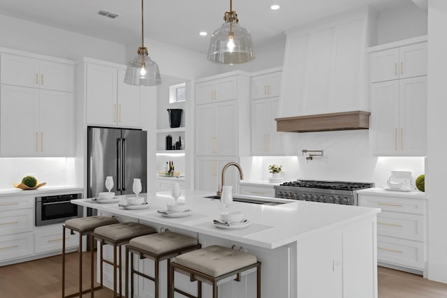 317 Rusk St, Roanoke, TX 76262 - kitchen with stainless steel appliances, light wood-style flooring, white cabinets, a kitchen island with sink, and pendant lighting