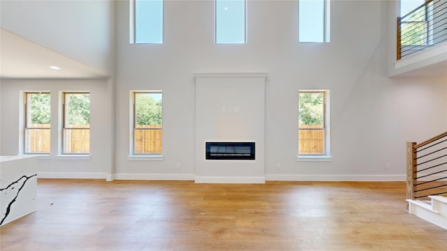 6857 Rutland Dr, Arlington, TX 76002 - unfurnished living room featuring a high ceiling, stairway, light wood-style flooring, and healthy amount of natural light