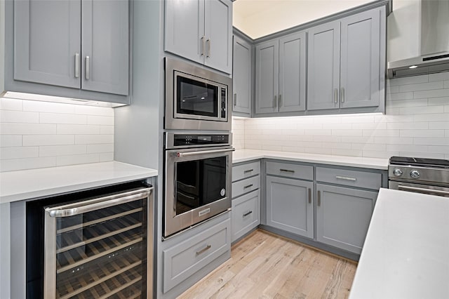 5067 Gaston Ave, Dallas, TX 75214 - kitchen featuring gray cabinets, stainless steel appliances, beverage cooler, wall chimney exhaust hood, and light wood finished floors