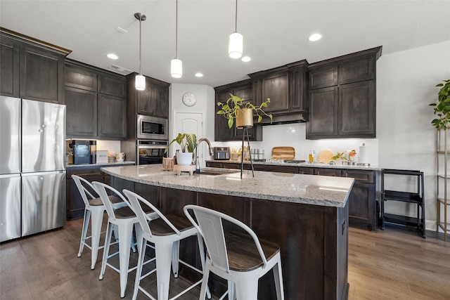 205 Big Creek Loop, Hewitt, TX 76643 - kitchen with stainless steel appliances, wood finished floors, a breakfast bar, light stone counters, and a kitchen island with sink