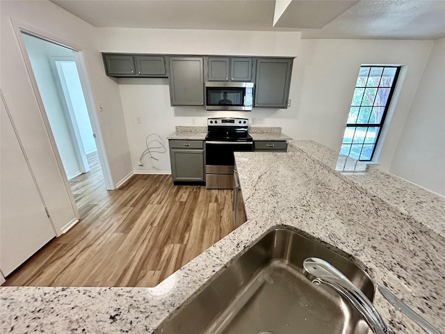3913 Longstraw Dr, Fort Worth, TX 76137 - kitchen featuring stainless steel appliances, light wood finished floors, light stone countertops, baseboards, and gray cabinetry