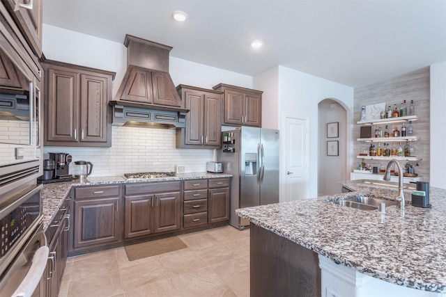 704 Granite Shoals Dr, Mckinney, TX 75071 - kitchen with stainless steel appliances, premium range hood, arched walkways, a sink, and dark brown cabinets
