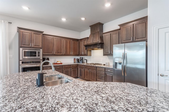 704 Granite Shoals Dr, Mckinney, TX 75071 - kitchen featuring appliances with stainless steel finishes, premium range hood, a sink, decorative backsplash, and dark brown cabinets