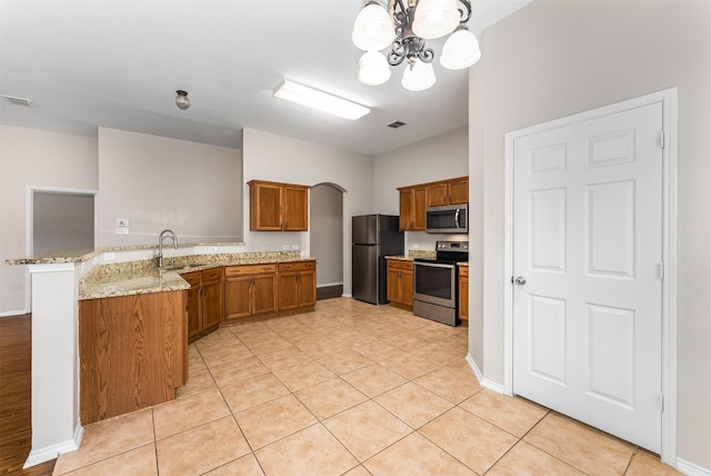 203 Mustang Trl, Celina, TX 75009 - kitchen featuring appliances with stainless steel finishes, brown cabinets, a peninsula, a sink, and a chandelier