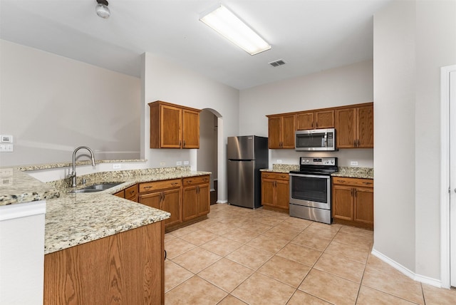 203 Mustang Trl, Celina, TX 75009 - kitchen featuring appliances with stainless steel finishes, a sink, light tile patterned flooring, arched walkways, and brown cabinetry