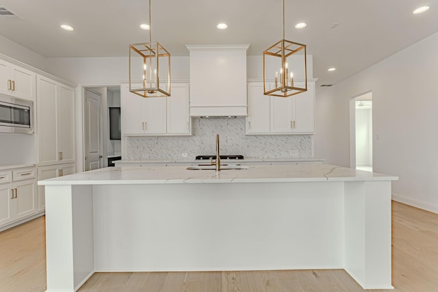 14448 Walsh, Aledo, TX 76008 - kitchen with premium range hood, stainless steel microwave, decorative backsplash, an island with sink, and light stone counters