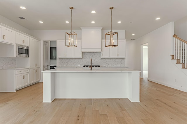 14448 Walsh, Aledo, TX 76008 - kitchen featuring stainless steel microwave, tasteful backsplash, light countertops, an island with sink, and white cabinetry