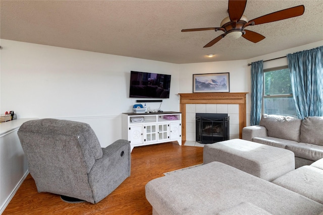13412 Dove Ranch Rd, Fort Worth, TX 76262 - living room featuring wood finished floors, ceiling fan, a textured ceiling, a tiled fireplace, and baseboards