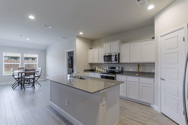 704 Griffith Park Trl, Alvarado, TX 76009 - kitchen with appliances with stainless steel finishes, a sink, white cabinets, light wood-type flooring, and an island with sink