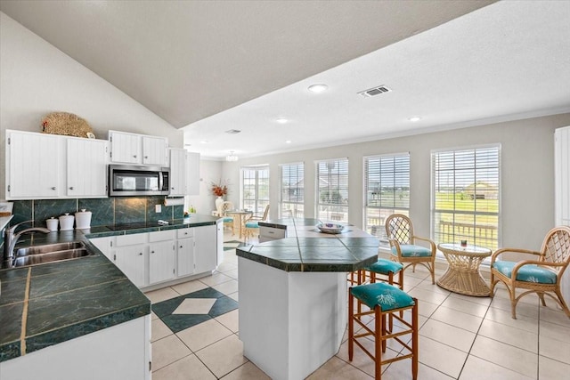 970 Gulfview Dr, Crystal Beach, TX 77650 - kitchen featuring a sink, stainless steel microwave, a breakfast bar area, backsplash, and light tile patterned floors