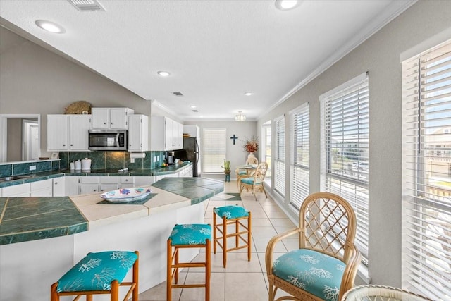 970 Gulfview Dr, Crystal Beach, TX 77650 - kitchen with stainless steel microwave, tasteful backsplash, white cabinets, light tile patterned flooring, and a breakfast bar area