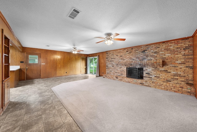 1804 Posey Ln, Sulphur Springs, TX 75482 - unfurnished living room featuring ceiling fan, wooden walls, a textured ceiling, brick wall, and a wood stove