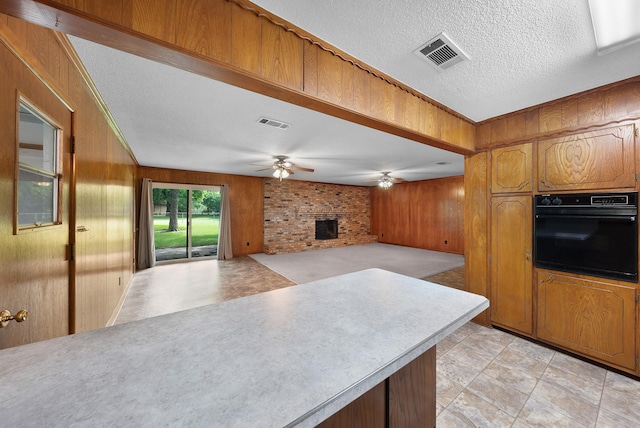 1804 Posey Ln, Sulphur Springs, TX 75482 - kitchen featuring black oven, wood walls, a ceiling fan, brown cabinets, and light countertops