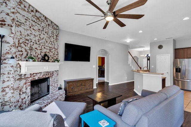 107 Oak Hollow Ln, Red Oak, TX 75154 - living room featuring ceiling fan, arched walkways, dark wood-type flooring, a fireplace with raised hearth, and a chandelier