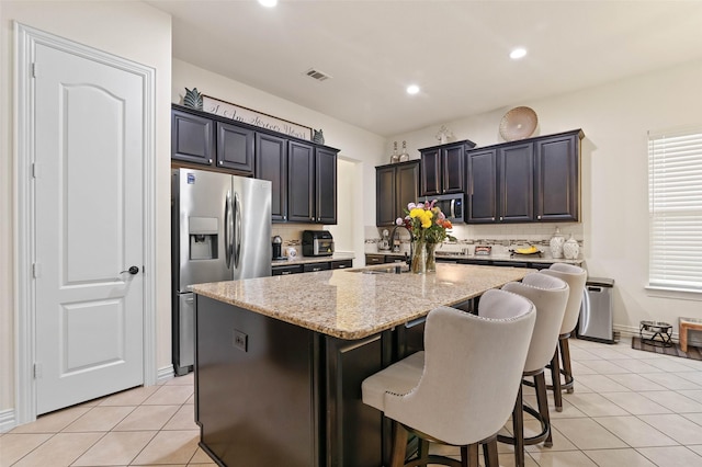 12341 Payne St, Frisco, TX 75033 - kitchen featuring stainless steel appliances, light tile patterned flooring, backsplash, light stone countertops, and a center island with sink