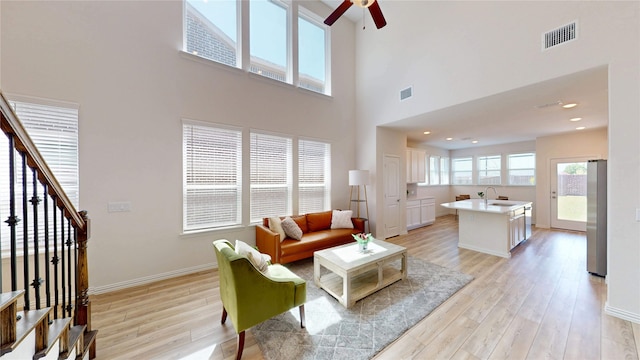 2753 Henson Ln, Garland, TX 75040 - living room featuring light wood-type flooring, a high ceiling, a ceiling fan, baseboards, and stairs