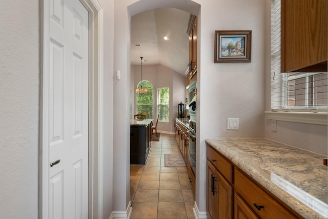 1869 Rio Blanco Dr, Frisco, TX 75033 - kitchen with arched walkways, brown cabinetry, lofted ceiling, light tile patterned floors, and light stone counters