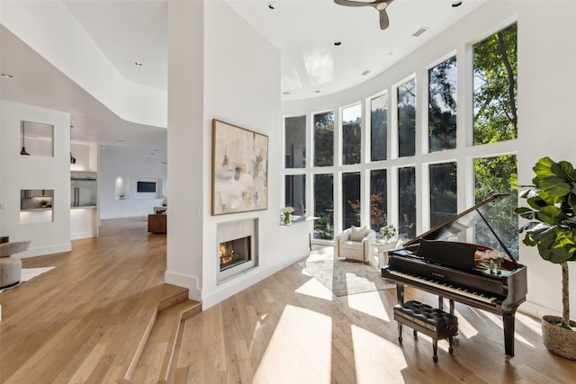6617 Shady Creek Cir, Plano, TX 75024 - sitting room with healthy amount of natural light, a warm lit fireplace, a towering ceiling, ceiling fan, and wood finished floors