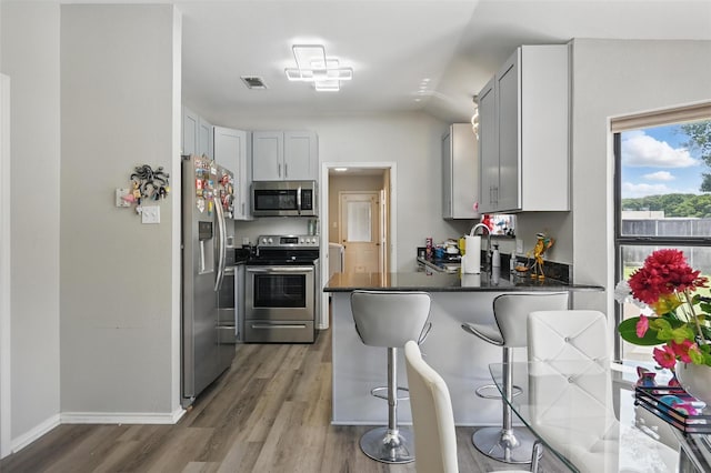 2701 Mims St, Fort Worth, TX 76112 - kitchen with appliances with stainless steel finishes, a peninsula, a kitchen bar, wood finished floors, and dark countertops