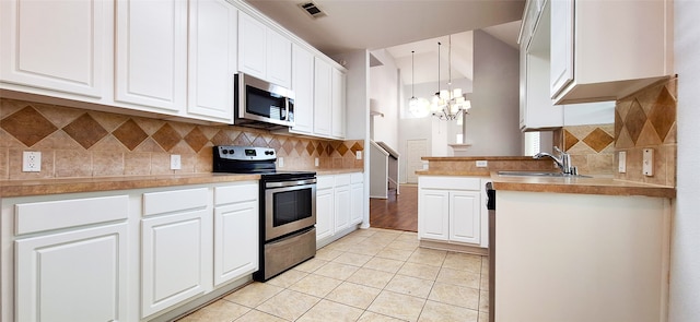 6731 Canterbury Dr, Frisco, TX 75035 - kitchen with stainless steel appliances, a sink, a chandelier, light tile patterned floors, and white cabinets