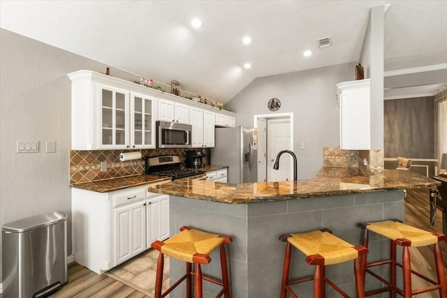 810 W Lonesome Dove Trl, Arlington, TX 76001 - kitchen with appliances with stainless steel finishes, a breakfast bar area, tasteful backsplash, glass insert cabinets, and a peninsula