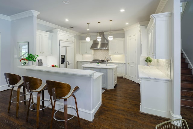 2900 Amherst Ave, University Park, TX 75225 - kitchen featuring wall chimney range hood, paneled built in refrigerator, a center island with sink, a peninsula, and backsplash