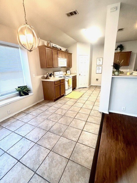 8309 Horse Whisper Ln, Fort Worth, TX 76131 - kitchen featuring white appliances, a chandelier, brown cabinets, lofted ceiling, and light countertops