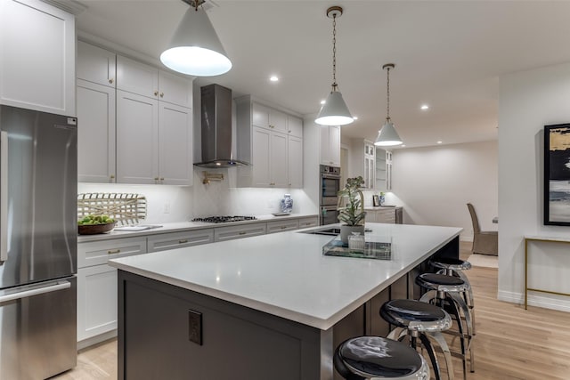 11207 Dwarfs Cir, Dallas, TX 75229 - kitchen featuring appliances with stainless steel finishes, wall chimney range hood, an island with sink, light wood finished floors, and recessed lighting