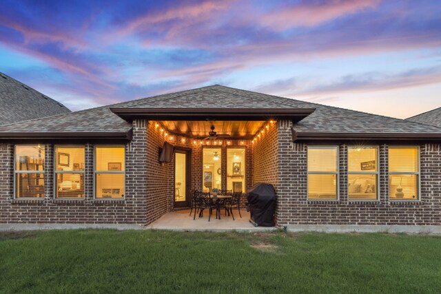 10113 Warberry Trl, Fort Worth, TX 76131 - back of property at dusk featuring brick siding, roof with shingles, ceiling fan, a lawn, and a patio