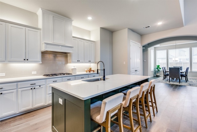 1421 Benavites Dr, Little Elm, TX 75068 - kitchen featuring a sink, arched walkways, stainless steel gas cooktop, a center island with sink, and light wood finished floors