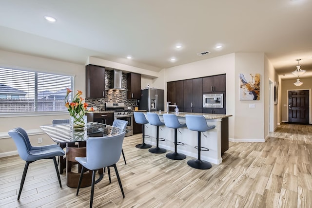 3446 Kirby Ln, Forney, TX 75126 - kitchen featuring appliances with stainless steel finishes, wall chimney exhaust hood, a breakfast bar area, dark brown cabinetry, and decorative backsplash