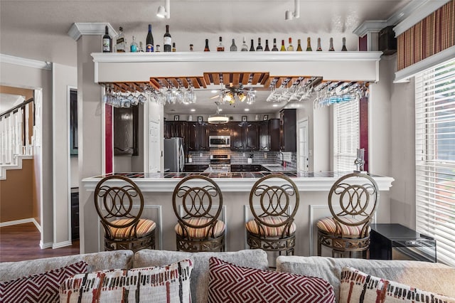 7705 Marble Canyon Ct, Fort Worth, TX 76137 - kitchen with appliances with stainless steel finishes, dark brown cabinetry, a breakfast bar, backsplash, and ornamental molding