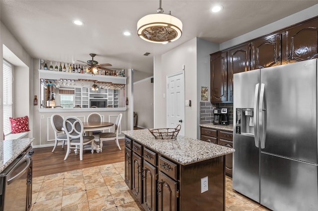 7705 Marble Canyon Ct, Fort Worth, TX 76137 - kitchen featuring appliances with stainless steel finishes, a ceiling fan, decorative backsplash, dark brown cabinetry, and a center island