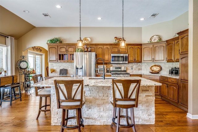 140 Daisey Ln, Justin, TX 76247 - kitchen featuring appliances with stainless steel finishes, an island with sink, brown cabinets, backsplash, and a breakfast bar