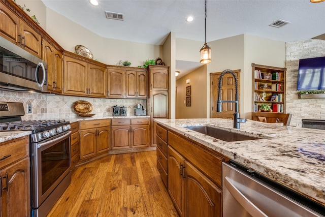 140 Daisey Ln, Justin, TX 76247 - kitchen featuring appliances with stainless steel finishes, a sink, wood finished floors, light stone countertops, and brown cabinetry