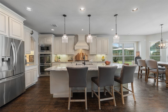 760 Ascot Ct, Prosper, TX 75078 - kitchen with appliances with stainless steel finishes, custom range hood, decorative backsplash, light stone counters, and a kitchen island with sink
