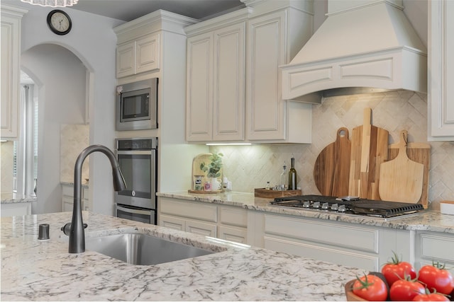 760 Ascot Ct, Prosper, TX 75078 - kitchen featuring custom range hood, appliances with stainless steel finishes, arched walkways, decorative backsplash, and light stone countertops