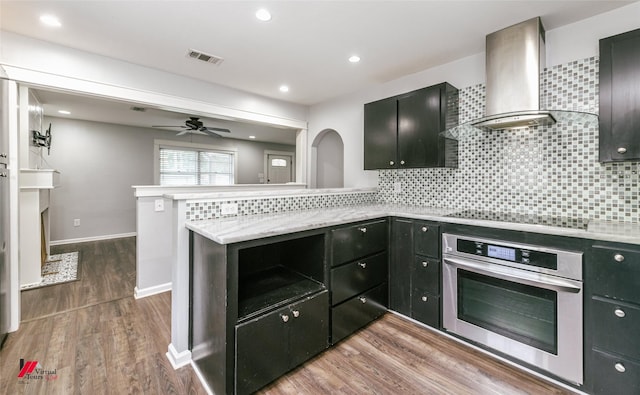 9472 Ranch Ln, Shreveport, LA 71106 - kitchen with oven, wall chimney range hood, black electric cooktop, backsplash, and ceiling fan