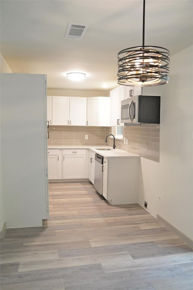 7810 Larchridge Dr, Dallas, TX 75232 - kitchen featuring appliances with stainless steel finishes, a sink, decorative backsplash, white cabinetry, and light wood finished floors