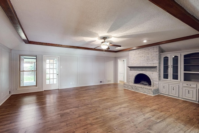 1308 Warwick St, Garland, TX 75040 - unfurnished living room featuring a textured ceiling, ceiling fan, a decorative wall, a brick fireplace, and wood finished floors