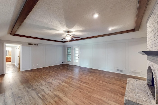 1308 Warwick St, Garland, TX 75040 - unfurnished living room with a decorative wall, a textured ceiling, a ceiling fan, a fireplace, and wood finished floors
