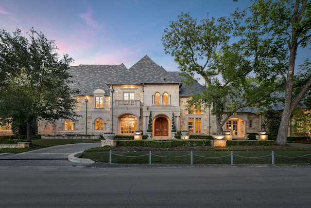 9996 Hollow Way Rd, Dallas, TX 75220 - french country inspired facade featuring stone siding, a balcony, french doors, a fenced front yard, and a high end roof