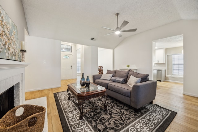 226 E Ridgegate Dr, Garland, TX 75040 - living room featuring vaulted ceiling, ceiling fan, light wood-style flooring, a brick fireplace, and a textured ceiling
