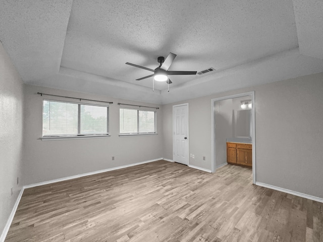 539 Mel Ct, Euless, TX 76039 - unfurnished bedroom featuring a tray ceiling, a textured ceiling, light wood-type flooring, baseboards, and ensuite bath