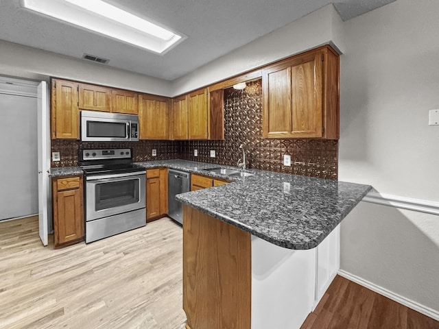 539 Mel Ct, Euless, TX 76039 - kitchen with stainless steel appliances, a peninsula, brown cabinets, a sink, and tasteful backsplash